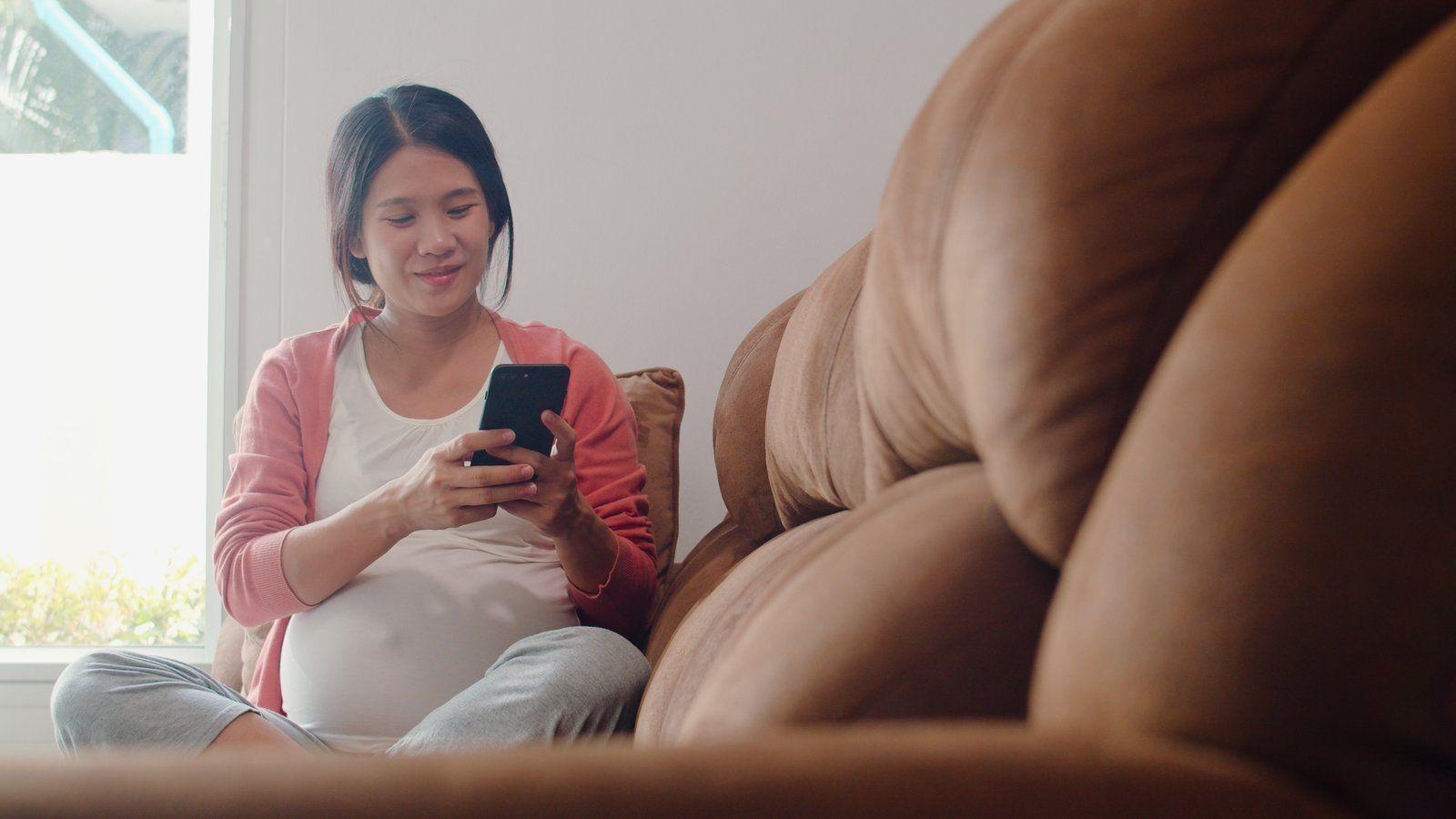 Femme enceinte consultant son téléphone sur un canapé